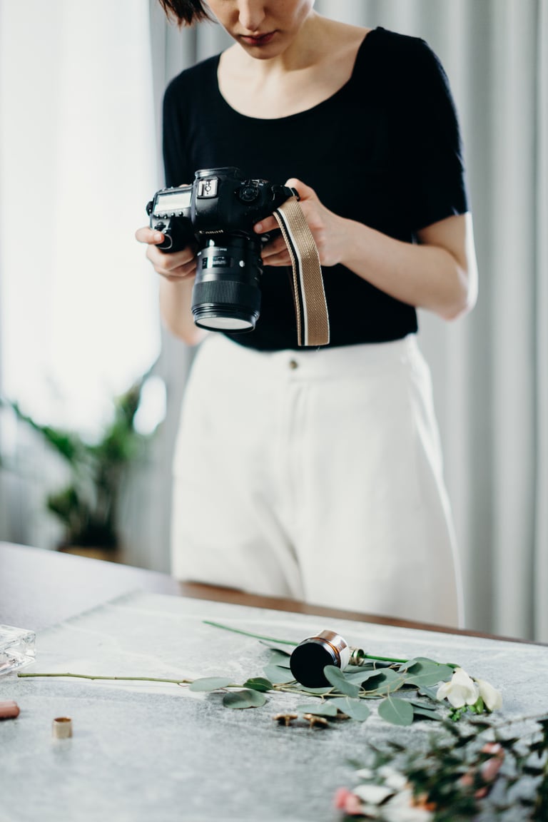 Woman Wearing Black Shirt Taking Photos Of Flowers On Top Of Table